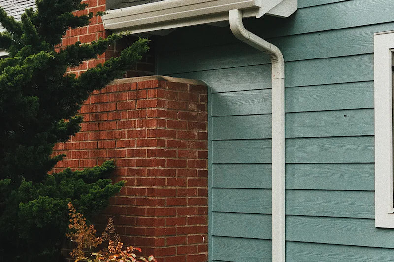 Blue lap siding meeting a red brick chimney, with a white downspout