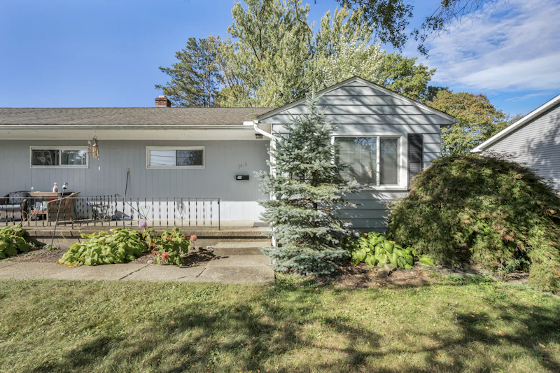 Light gray ranch house with a front porch and a blue spruce in the yard