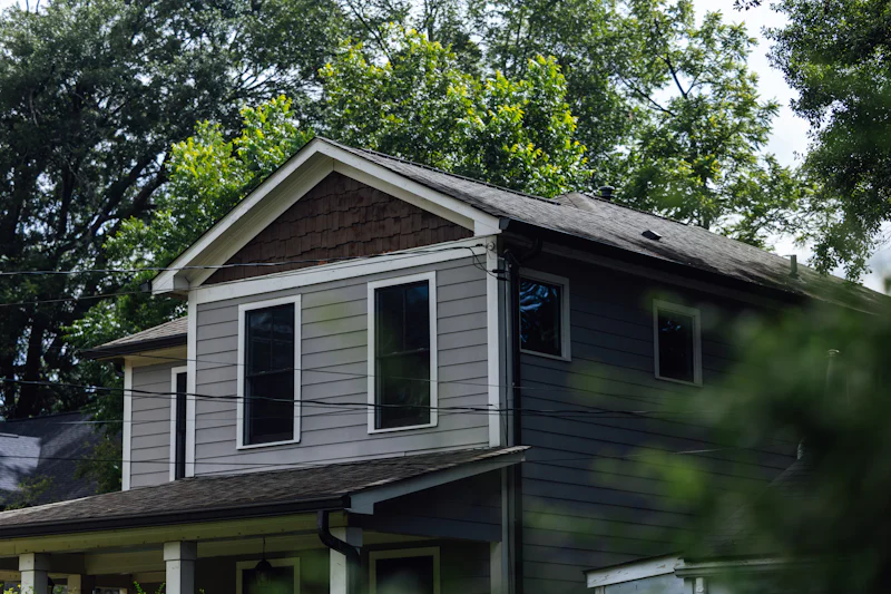 Gray two-story house with mixed siding among green trees