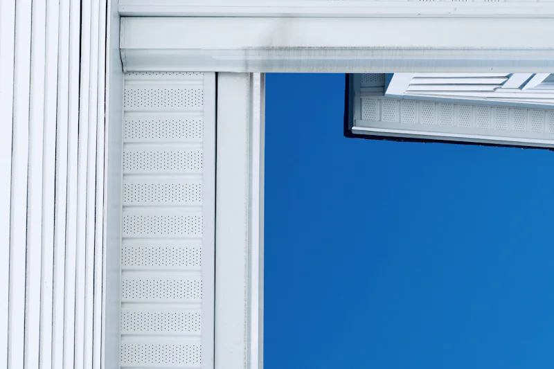 White vented soffit panels and trim at a roof corner against a blue sky