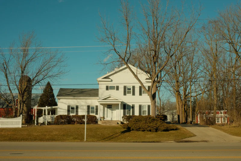 White two-story colonial house set back from the road behind bare trees